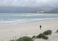 Lorraine is standing on a beach, facing the sea, with her arms wide open
